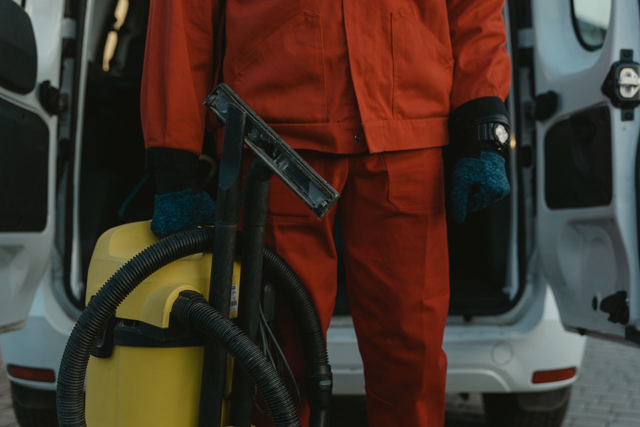 services-03 A professional cleaner in a red uniform holding a vacuum near a van, ready for service.